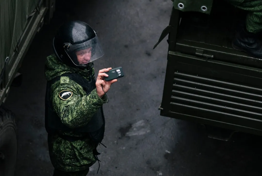 man in green and black camouflage jacket holding black smartphone